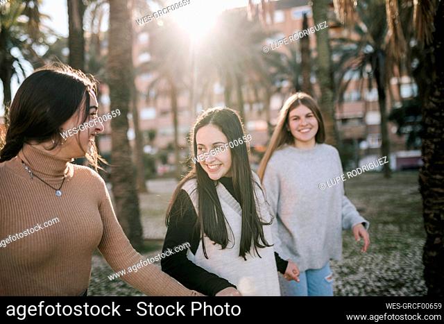 Happy female friends holding hands while walking on footpath in park