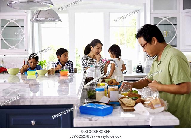 Family Having Breakfast And Making Lunches In Kitchen