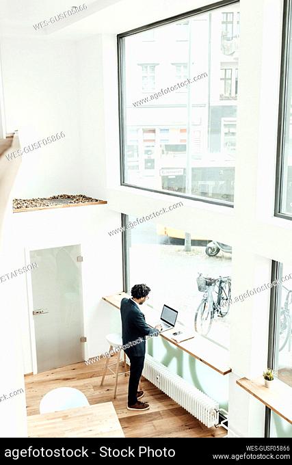 Male entrepreneur using laptop while standing by glass window in office