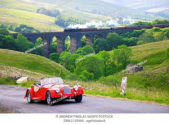 "Red car in front of viaduct with steam train LMS Stanier Class 8F """"Fellsman"""" 48151, pulling carriages on Dent Head Viaduct Yorkshire Dales National Park...