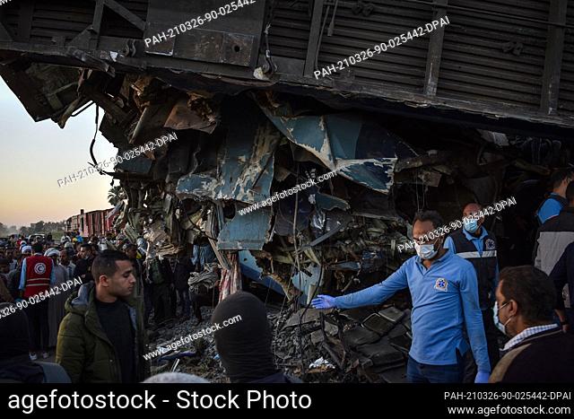 26 March 2021, Egypt, Tahta: Medial workers and people gather to inspect damaged train cars after two passenger trains collided near Tahta in Sohag Governorate