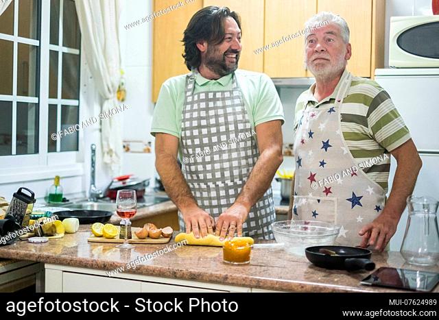 Two man at work in the kitchen adult and senior. Son and father cook together with smilies and surprise at home. daily family life concept
