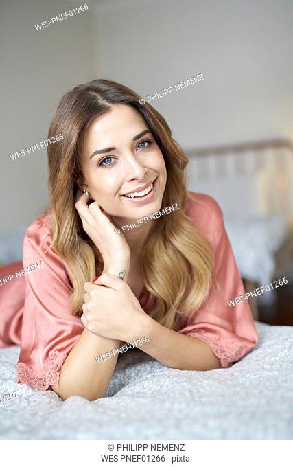 Portrait of smiling young woman in dressing gown lying in bed