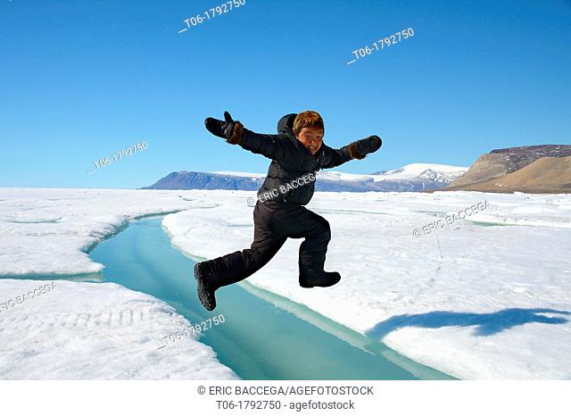 Young Inuit boy jumping over a crack on ice floe Ellesmere island, Nanavut, Canada