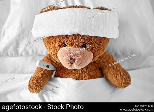 ill teddy bear with bandage and thermometer in bed