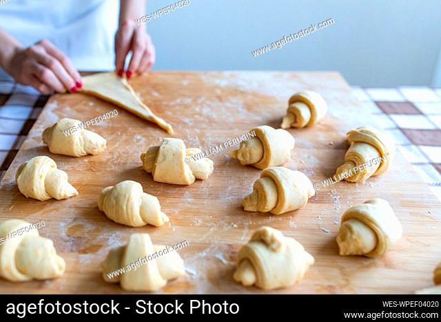 Woman making croissants on cutting board in kitchen