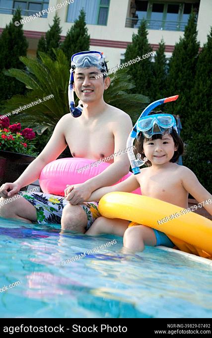 Portrait of father and son in snorkeling gear sitting by the edge of the pool