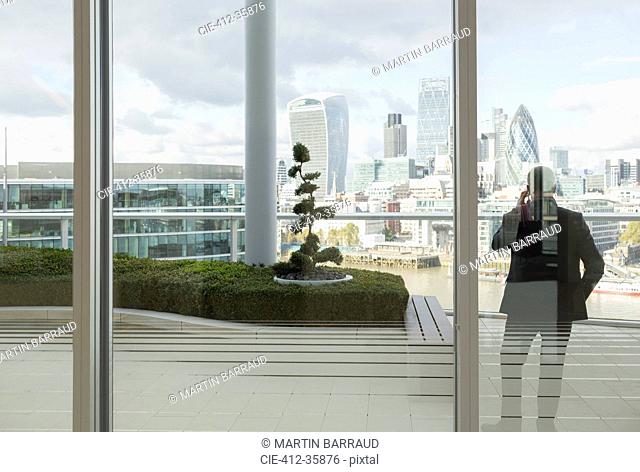 Businessman talking on cell phone on balcony with urban city view, London, UK