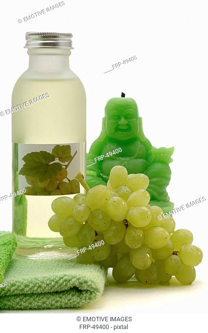 Traubenkernöl aus weißen Trauben, mit einem grünen Handtuch, weißen Weintrauben und einer grünen Buddha-Kerze