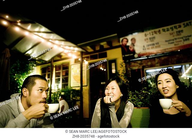 Three friends enjoying coffee and laughter at an outdoor cafe in Los Angeles, California