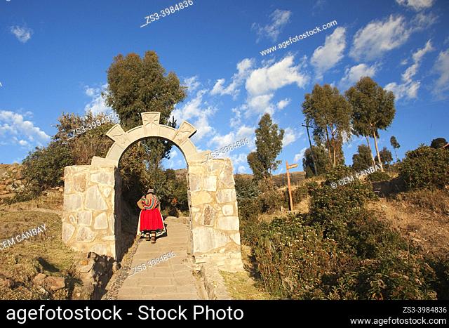 Indigenous woman in traditional dress passing through a stone arch and walking up to her house, Amantani Island, Titicaca Lake, Puno Region, Peru, South America