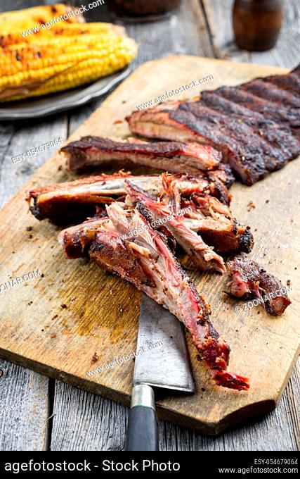 Barbecue spare ribs St Louis cut with hot rub and corn as closeup on a wooden cutting board