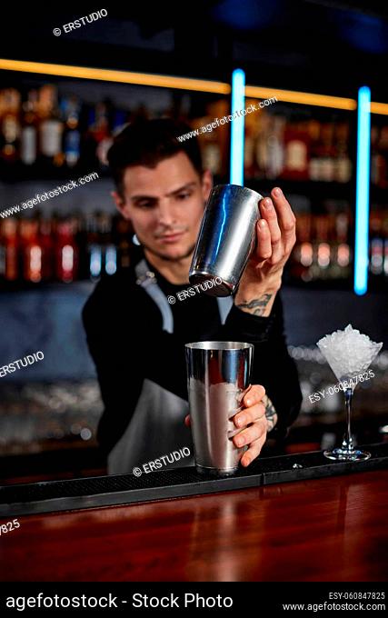 handsome barman is making cocktail with steel shaker at the bar counter