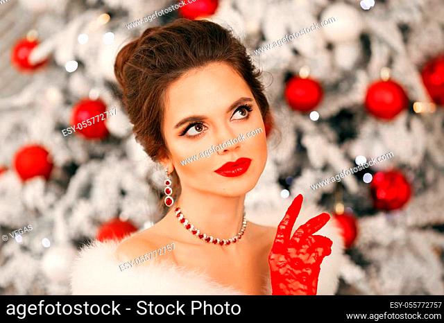 Winter portrait of Elegant woman with ruby jewelry set and red gloves. Beautiful brunette lady with wedding hairstyle, beauty makeup wears posing over xmas tree...