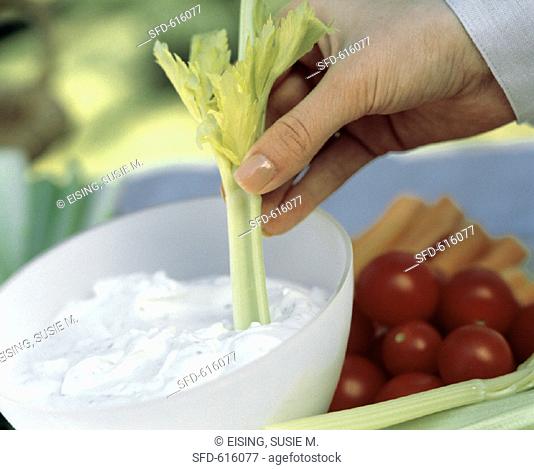 A Hand Dipping a Celery Stick into Dip