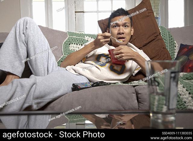 Lazy man eating on sofa and watching television