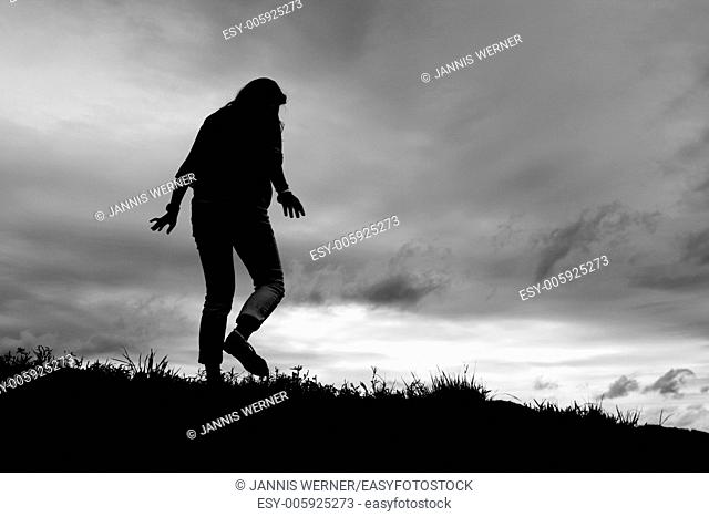 Silhouette of girl walking away on a grassy hill slope