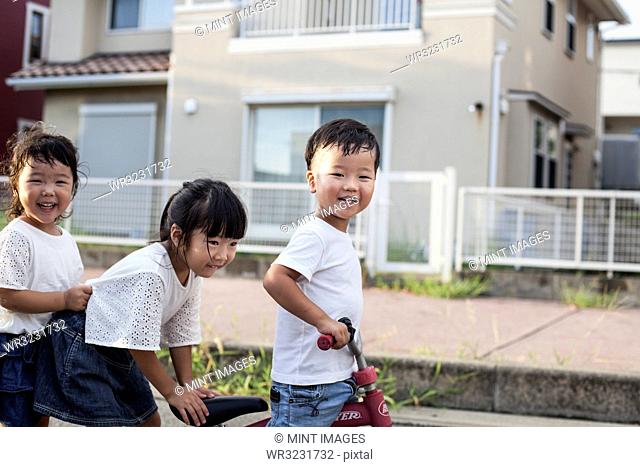 Portrait of two Japanese girls and boy playing on street with a bicycle, smiling at camera