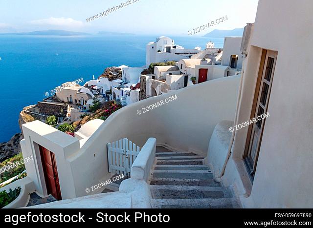 Stairs down to traditional white washed Greek houses along the coastline with blue ocean in Oia, Santorini, Greece