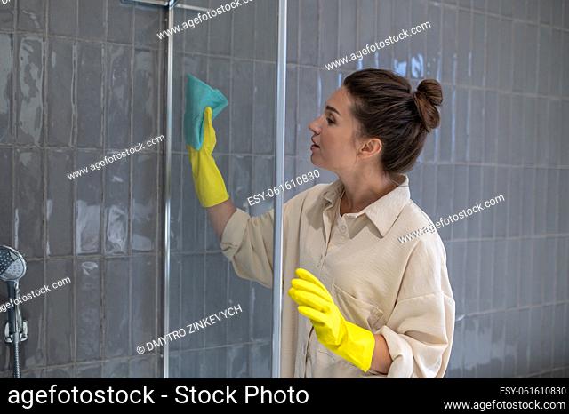 Hygiene. Young woman cleaning the sahower cabin and looking involved