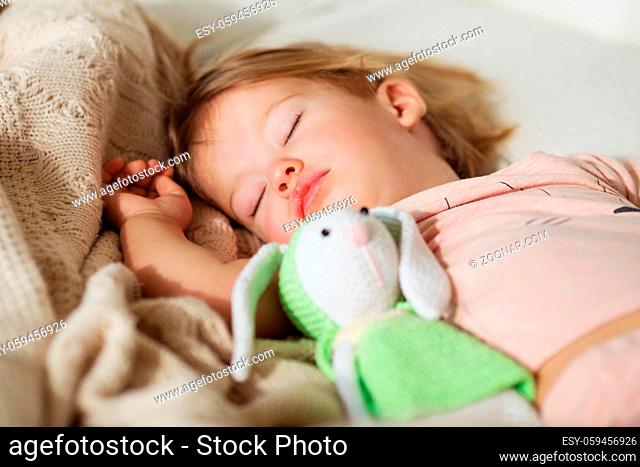 Sleeping little girl. Carefree sleep little baby with a soft toy on the bed. Close-up portrait of a beautiful sleeping child on knitted blanket