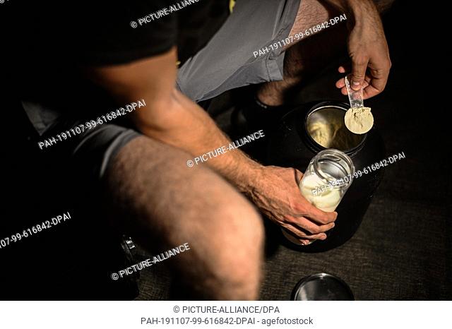 03 November 2019, Bavaria, Ebing: ILLUSTRATION - A man mixes protein powder into his shaker (posed scene) after training