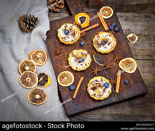 sweet cakes with white cream and chocolate powder on a brown wooden board, top view