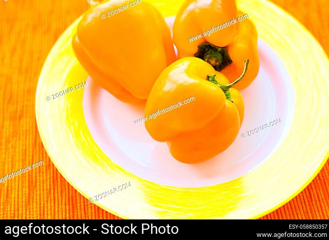 Three bright yellow peppers on a plate close up