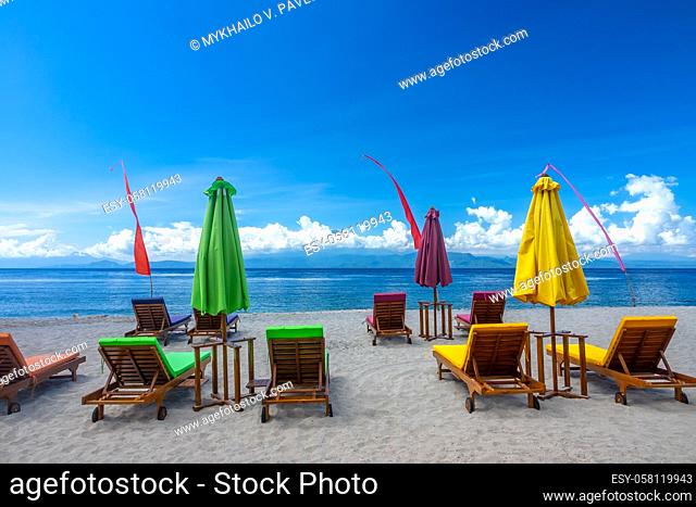 Tropical sandy beach and blue sky with clouds. Empty sunbeds and closed beach umbrellas