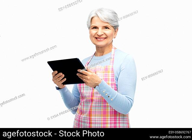 smiling senior woman in apron with tablet computer