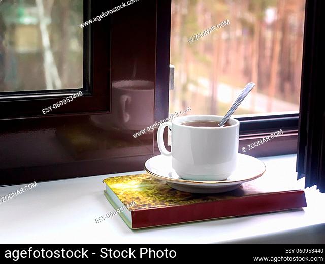 On the windowsill at the open window, a Cup of tea and a book, outside the window a view of the autumn Park