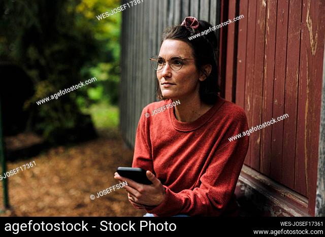 Thoughtful woman with mobile phone sitting in doorway