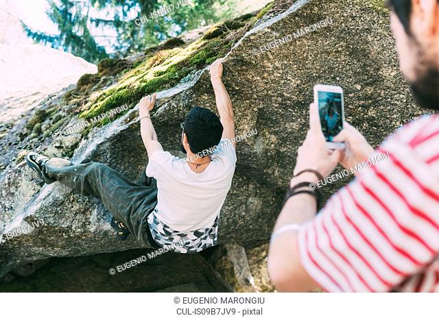 Male boulderer photographing friend with smartphone, Lombardy, Italy