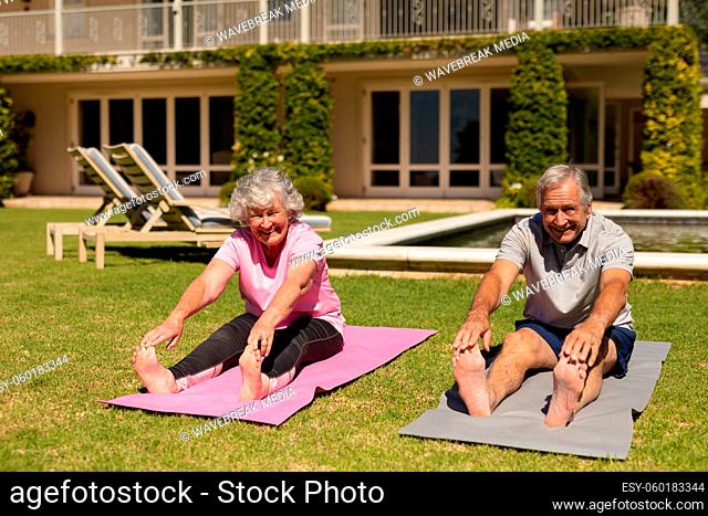 Portrait of senior caucasian couple practicing yoga, stretching in sunny garden