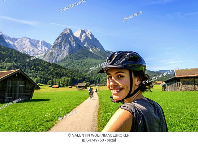 Female cyclist with helmet on bike tour, in the back Zugspitze, Tegernauweg, near Grainau, crossing the Alps, Garmisch-Partenkirchen, Upper Bavaria, Bavaria