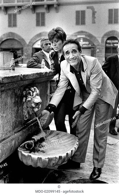 Italian actor and dubber Arnoldo Foà playing with the water of a fountain. Behind him, his Italian wife Ludovica Volpe. Florence, 1971