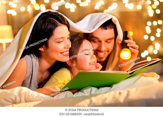 happy family reading book in bed at night at home
