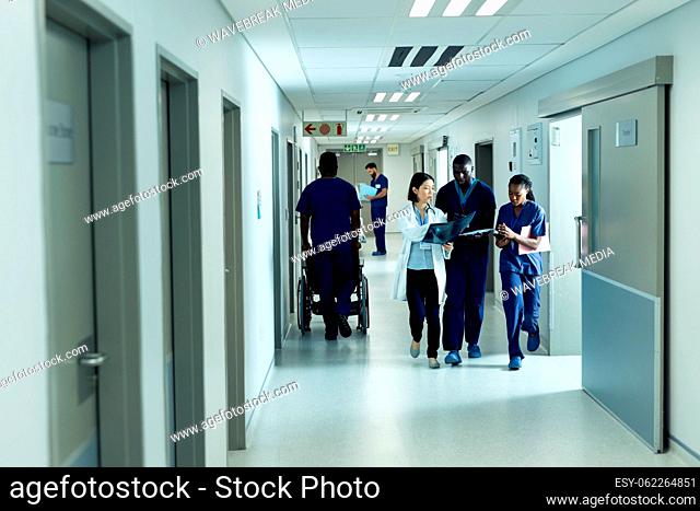 Diverse female doctor and healthcare workers discussing and walking in hospital corridor, copy space