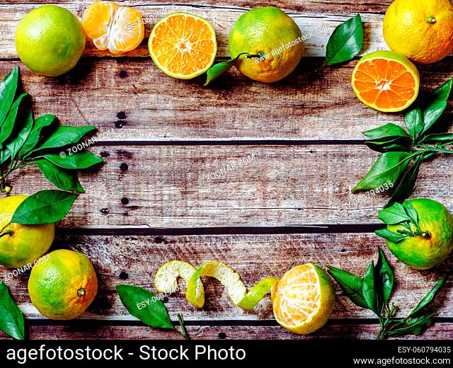 Green mandarines on old wooden background. Fresh ripe half, whole and peeled green tangerines with leaves, top view or flat lay