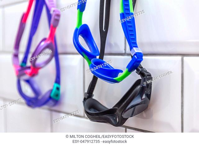 Family of swimming goggles hanging on a tiled wall