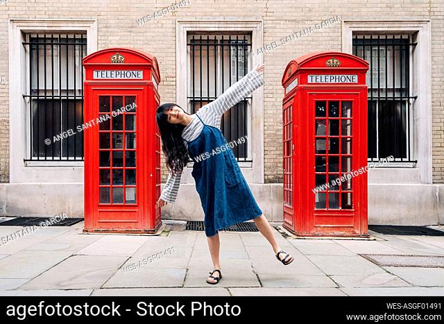 Woman with arms outstretched balancing in front of telephone booth