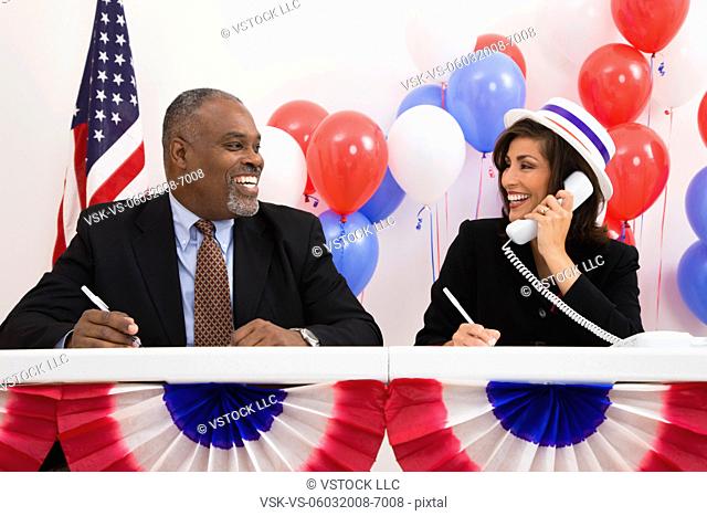 USA, Illinois, Metamora, Smiling man and woman at polling place table, red and blue balloons in background