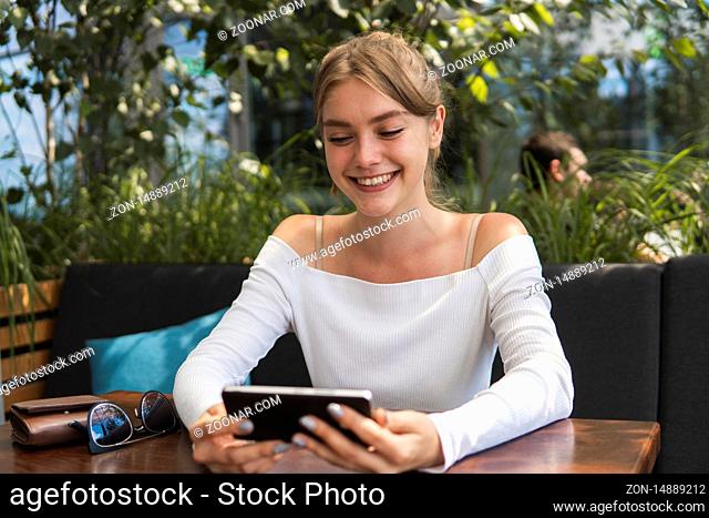Photo of beautiful lady sitting in cafe and making selfie with a smart phone. Portrait of young smiling student girl make video call from smartphone to her best...
