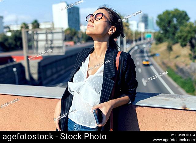 Young woman wearing sunglasses standing while leaning on retaining wall