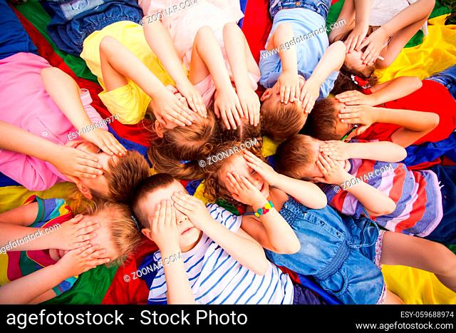 Top view children covering faces by hands, laying on a floor very closely, touching their heads and hair. Kids trying to relax after active games