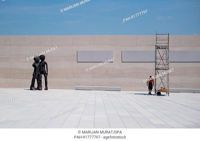 dpatop - A construction worker stands under the shadow of a scaffolding, while the 2012 bronce sculpture ""BDM (Group of girls)"" stands nearby