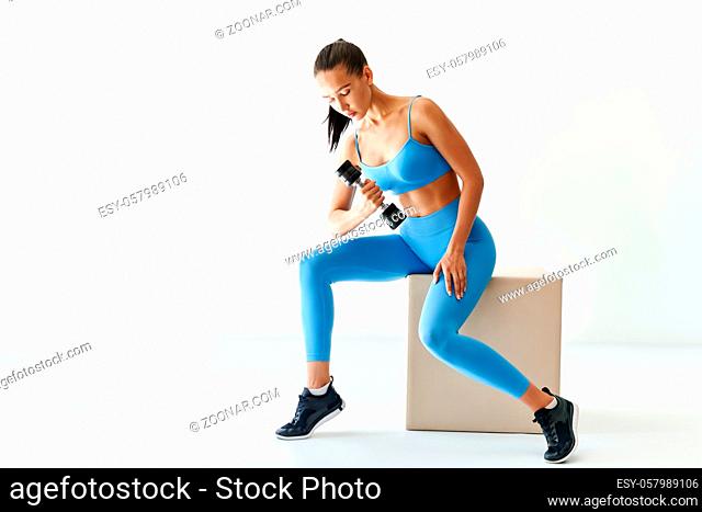 Sporty woman in sportswear doing exercise with dumbbells on white background with copy space. Strength and motivation concept