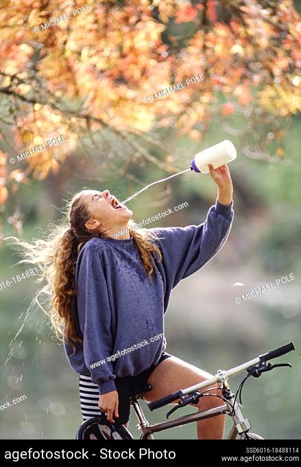 Young woman stopped on her bicycle squirting water into her mouth from water bottle