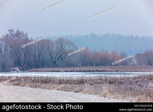 Winter european landscape with frozen pond covered with snow and heavy snowfall storm with falling snowflakes. Christmas winter concept