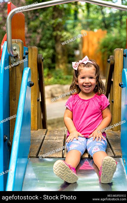 Portrait of happy little girl sitting on playground slide